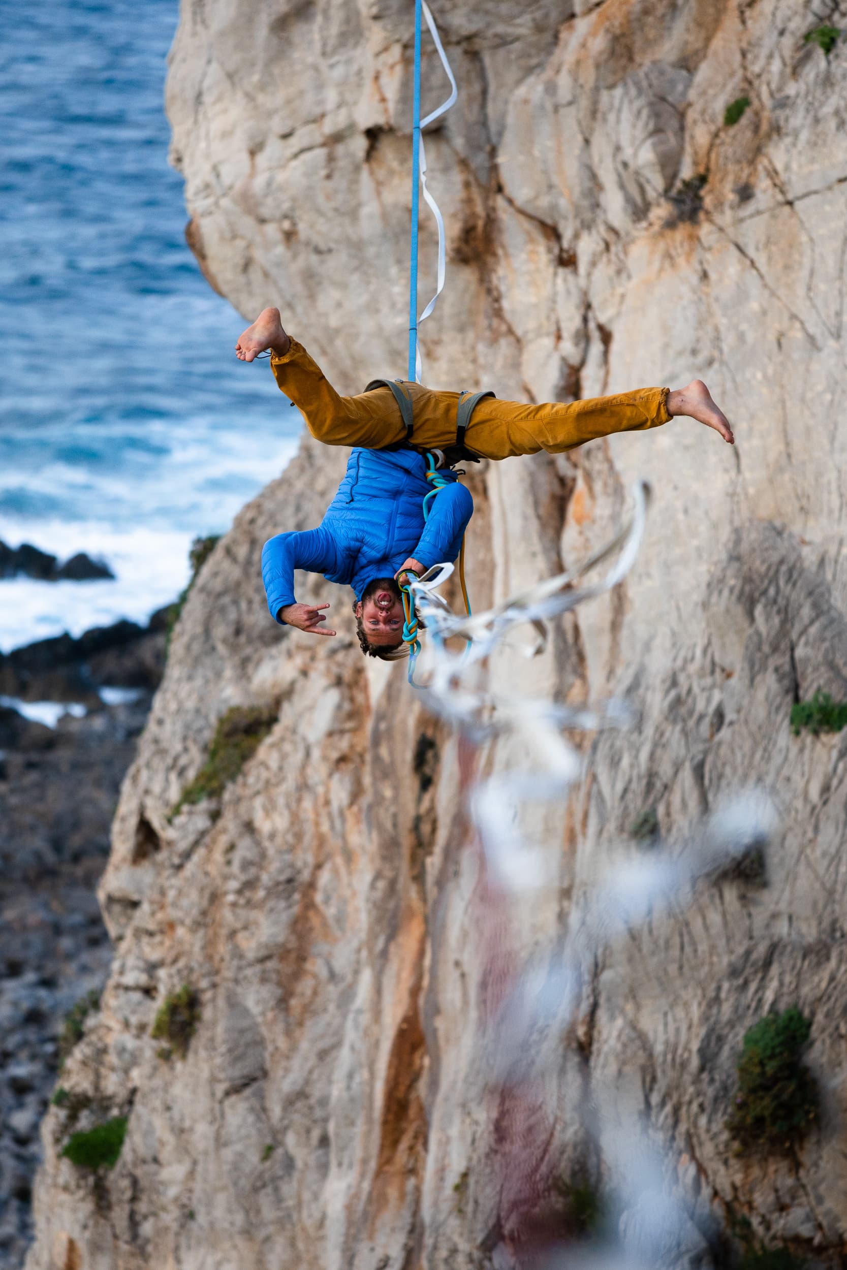 Alessandro appeso a testa in giù sotto una highline, su una parete di roccia sul mare